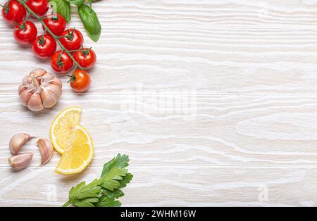 Composizione sana degli ingredienti alimentari con pomodori ciliegini freschi, erbe, spicchi d'aglio, spicchi di limone su dorso di legno bianco Foto Stock