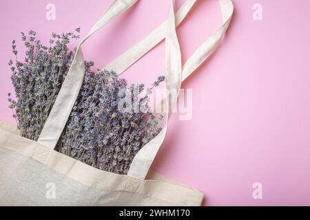 Bouquet di fiori di lavanda in borsa per shopper di lino eco beige su sfondo viola vista dall'alto. Romantica primavera o estate femminile Foto Stock