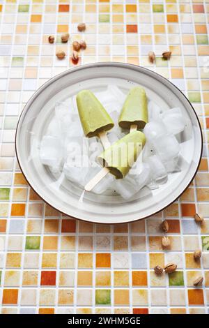 Pistacchio surgelato fatto in casa in ciotola di ghiaccio su tavola di tessere mosaico. Pop cicle rinfrescante, succo verde congelato sul bastone. Top vi Foto Stock