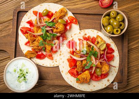 Cucina tradizionale greca Gyros: Pane Pita con verdure, carne, erbe, olive su tagliere rustico di legno con Tzatzi Foto Stock