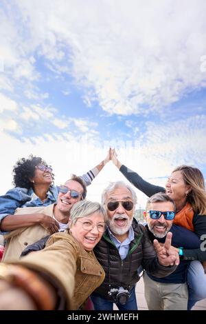 Gruppo di amici turistici maturi e divertenti che si mettono in posa con le mani unite in aria per scattare selfie. Foto Stock
