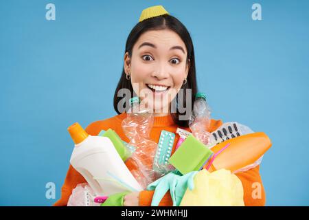 Ritratto di una donna coreana entusiasta, con bottiglie di plastica vuote, smistamento dei rifiuti, sorridente e dall'aspetto felice, isolata su BL Foto Stock