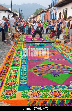 Antigua, Guatemala. Semana Santa, settimana Santa. Gli spettatori guardano mentre gli artisti mettono gli ultimi ritocchi su un alfombra (tappeto) di segatura colorata da decorare Foto Stock