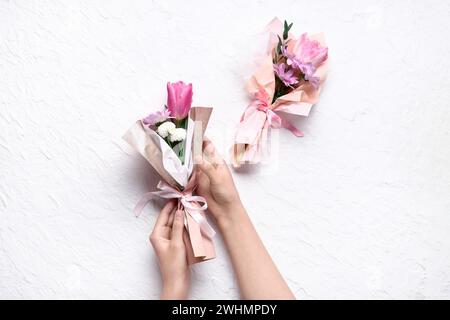 Mani femminili con piccoli mazzi di bellissimi fiori primaverili in carta da imballaggio su sfondo bianco. Giornata internazionale della donna Foto Stock