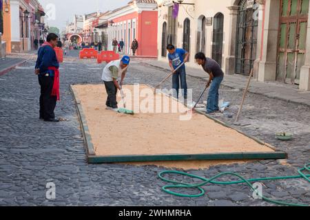 Antigua, Guatemala. Preparazione della base per segatura per un alfombra (tappeto) di fiori, aghi di pino e altri materiali tradizionali per decorare il stre Foto Stock