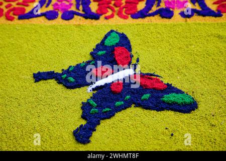 Antigua, Guatemala. Dettaglio farfalla su un alfombra (tappeto) di segatura colorata che decora la strada di fronte alla chiesa di la Merced prima del Foto Stock