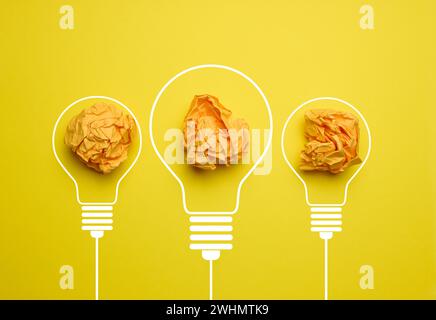 Sfere di carta schiacciate all'interno di una lampada elettrica su sfondo giallo. Concetto di nuove idee, brainstorming Foto Stock