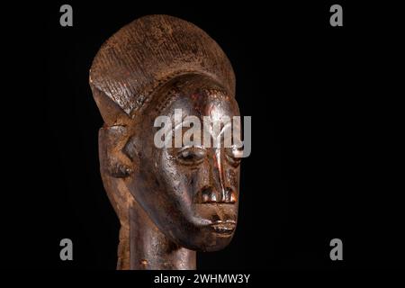 Una statua femminile africana scolpita in legno isolata sul nero. Arte tradizionale africana con forme e volumi equilibrati e bella patina marrone scuro. Foto Stock