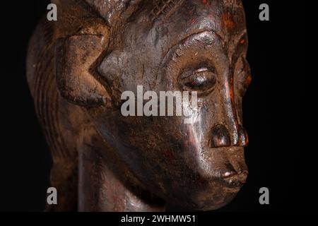 Ritratto di una statua femminile africana scolpita in legno isolata sul nero. Arte tradizionale africana con forme e volumi equilibrati e splendida patin nera Foto Stock