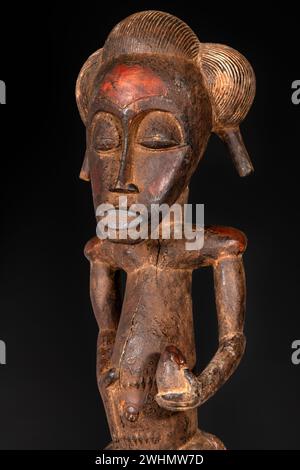 Primo piano di una figura Senufo maschio in legno della Costa d'Avorio con patina marrone isolata sul nero. Arte tribale africana, che mostra maestria artigianale a. Foto Stock