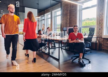 Un gruppo eterogeneo di professionisti collabora in un moderno centro di coworking startup, utilizzando un mix di supporti cartacei e. Foto Stock