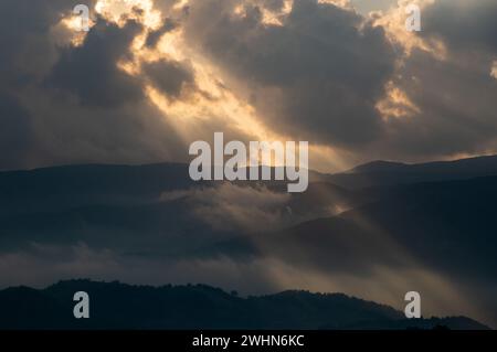 Il sole luminoso raggi di luce che brilla attraverso le nuvole scure sopra la montagna al tramonto. Cielo spettacolare in inverno Foto Stock