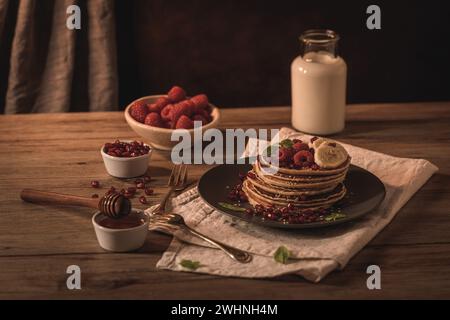 Pancake con lamponi, fette di banana, semi di melograno e miele Foto Stock