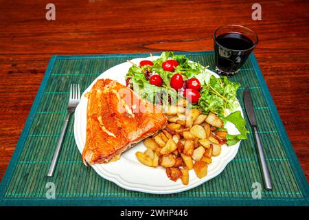 Primo piano di un piatto bianco di terracotta su una tovaglietta verde con un pezzo di salmone affumicato, patate fritte e lattuga con pomodori da snack, poi t Foto Stock