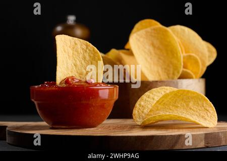 Patatine fritte in una ciotola di legno e una ciotola di salsa su un tavolo nero, spuntino Foto Stock