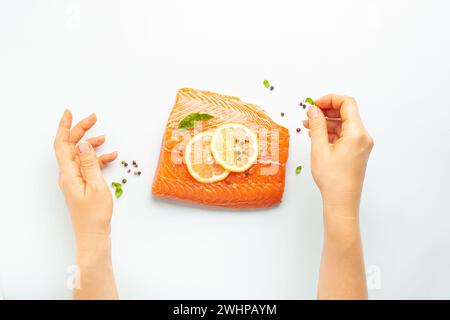 Condimento delle mani delle donne filetto di salmone fresco crudo marmorizzato isolato su sfondo bianco con limone, sale grosso, erbe verdi top vie Foto Stock