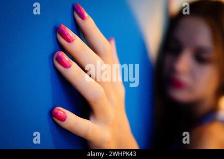 Mujer joven apoyada en una pared azul Foto Stock