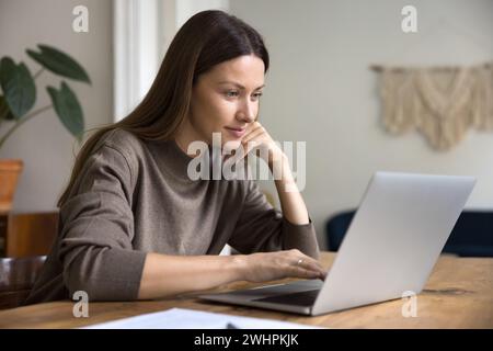 Donna professionale freelance positiva e pensiva che scrive su un notebook Foto Stock