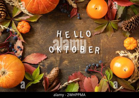 Ciao oktober, stagione autunnale. Biglietto d'auguri, foglie cadute, zucche e coni su una tavola di legno. Sfondo naturale autunnale Foto Stock