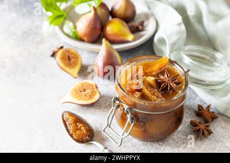 Confettura di fichi fatta in casa in un vaso di vetro con fichi freschi su un tavolo grigio chiaro. Conservazione del raccolto autunnale, cibo fermentato sano Foto Stock