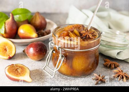 Confettura di fichi fatta in casa in un vaso di vetro con fichi freschi su un tavolo grigio chiaro. Conservazione del raccolto autunnale, cibo fermentato sano Foto Stock