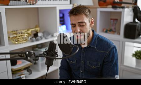 Bellissimo giovane ispanico, un artista serio con la barba, che si concentra mentre canta appassionatamente la sua canzone, eseguendo con un microfono in un indoo Foto Stock