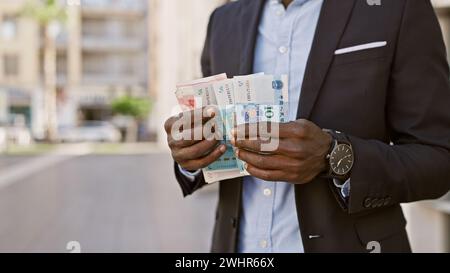 Uomo africano in tuta che conta lo yuan cinese all'aperto in un ambiente urbano. Foto Stock