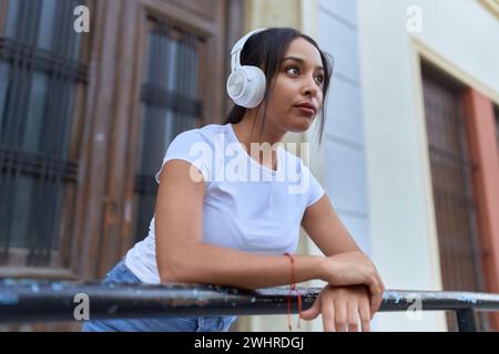 Giovane donna araba che ascolta musica appoggiata sulla balaustra per strada Foto Stock