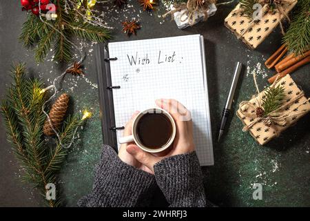 La donna scrive su un quaderno con una lista di oggetti vuoti e una tazza di caffè su un tavolo in pietra scura natalizia. Background degli obiettivi del nuovo anno. Piatto Foto Stock