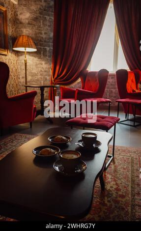 Poltrone rosse con tazze da caffè sul tavolo in un intimo interno classico. Antico soggiorno con tende rosse e poltrone. Sala del castello di Hogwarts. Foto Stock