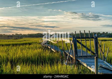 Vecchio molo in legno fatiscente nell'erba paludosa e nell'insenatura di Palweys Island, South Carolina, al tramonto Foto Stock
