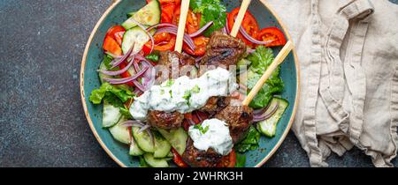 Spiedini grigliati di carne di manzo spiedini su bastoncini serviti con insalata di verdure fresche su piatto su sfondo rustico di cemento dall'alto. Foto Stock