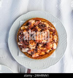 Piatto di polpo in stile galiziano, servito sul tipico piatto di legno; consiste in fette di polpo cotte, condite con olio d'oliva, paprika e sale Foto Stock