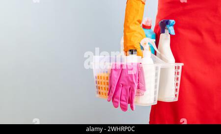 Persona che tiene in mano il cestello con materiali di consumo per la pulizia e indossa guanti Foto Stock