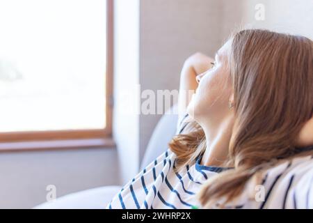 Donna che si rilassa vicino alla finestra godendosi la luce del sole Foto Stock