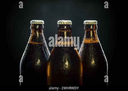 Tre bottiglie di birra fresca sul nero Foto Stock