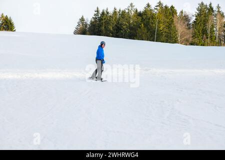 uno snowboarder con una felpa blu e un casco cavalcano su una pista innevata. Foto Stock