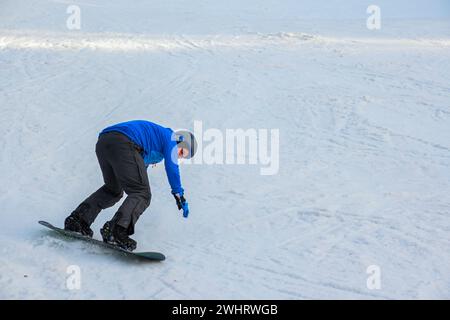 uno snowboarder con una felpa blu e un casco cavalcano su una pista innevata. Foto Stock