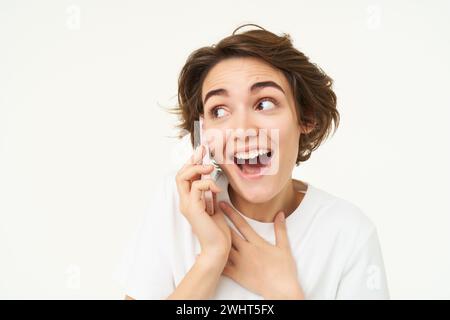 Ritratto di una bruna stupita sembra sorpreso mentre parla al telefono cellulare, risponde a una chiamata, stupita dalle grandi notizie e dallo shock mozzafiato Foto Stock