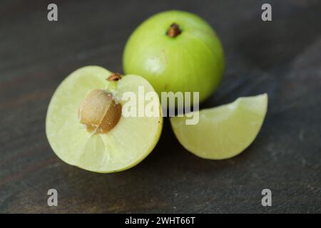 Primo piano della sezione fresca di Amla Berry con frutta intera su fondo di legno nero Foto Stock