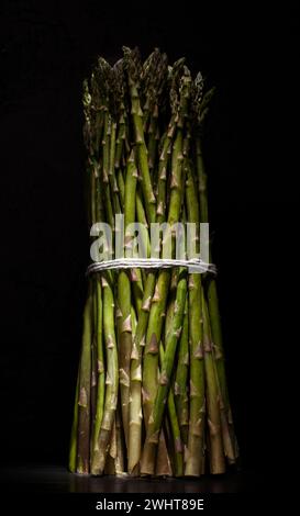 Lance di asparagi verdi elegantemente impacchettate con spago, presentate su un'elegante superficie nera Foto Stock