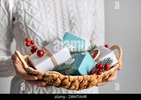 Donna che tiene in mano un cestino con regali di Natale avvolti in modo sostenibile, primo piano, attenzione selettiva. Decorazioni natalizie ecologiche Foto Stock