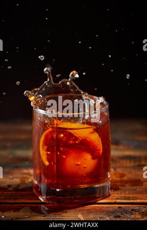 Cocktail alcolico Negroni o cocktail analcolico con spruzzo in bicchiere, bevanda con ghiaccio e buccia d'arancia come decorazione su legno Foto Stock