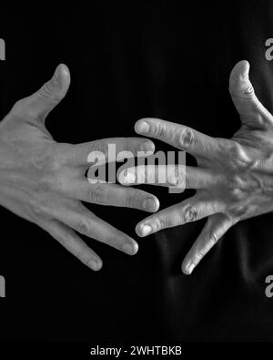 Le mani si intrecciano in un gesto di complessità su uno sfondo scuro Foto Stock