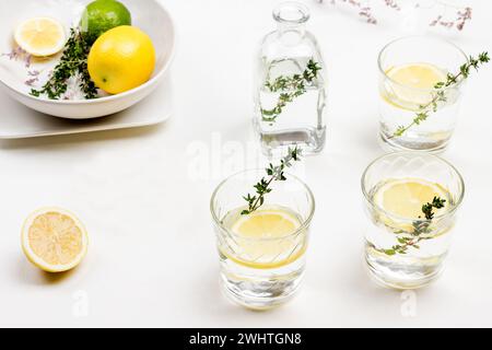 Bevanda al limone in bicchiere. Timo ciuffi in vetro. Limoni sul tavolo e in una ciotola di ceramica. Sfondo bianco. Vista dall'alto. Foto Stock