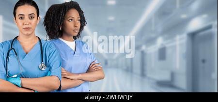 Due infermiere serie in scrub blu con braccia incrociate e stetoscopi Foto Stock