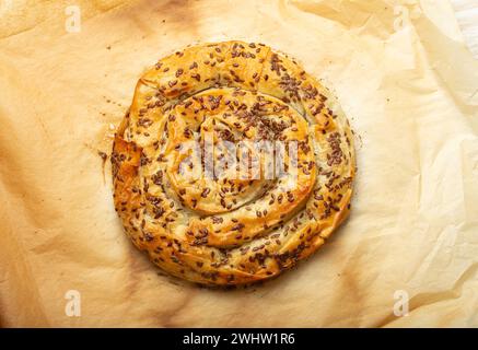 Burek appena sfornato in pasta filla con ripieno su carta da forno vista dall'alto. Tradizionale torta a spirale di Balka Foto Stock