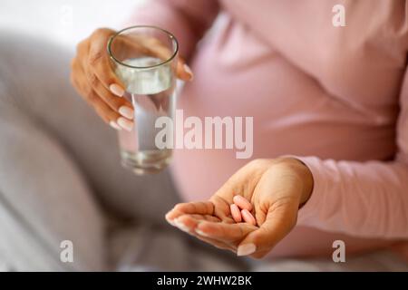 Vitamine e integratori prenatali. Donna incinta nera irriconoscibile che prende pillole a casa Foto Stock