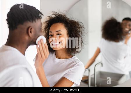 Felice coppia afroamericana si impegna nella cura del viso in bagno Foto Stock