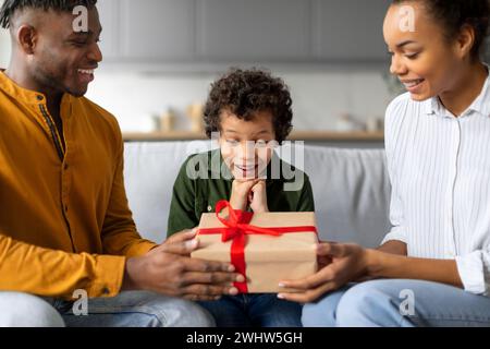 Bambino sorpreso che riceve un regalo dai genitori, felice momento familiare Foto Stock